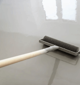 Close-up of a spiked roller being used to evenly spread self-leveling epoxy paint for floor application on a tile.