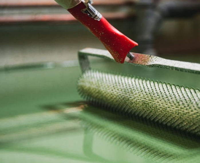 Close-up of a spiked roller being used to apply green epoxy paint for floor coating, ensuring an even, bubble-free finish on floor.