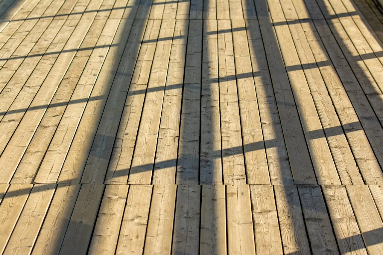 Close-up of outdoor wooden flooring with natural sunlight and shadows highlighting the grain and texture of the planks.