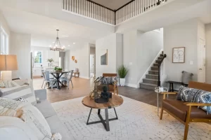 Modern open-concept living room with hardwood flooring, neutral décor, and carpeted staircase leading to the upper floor.