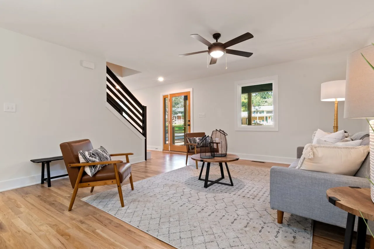 Modern open-concept living room with hardwood flooring, neutral décor, and carpeted staircase leading to the upper floor.